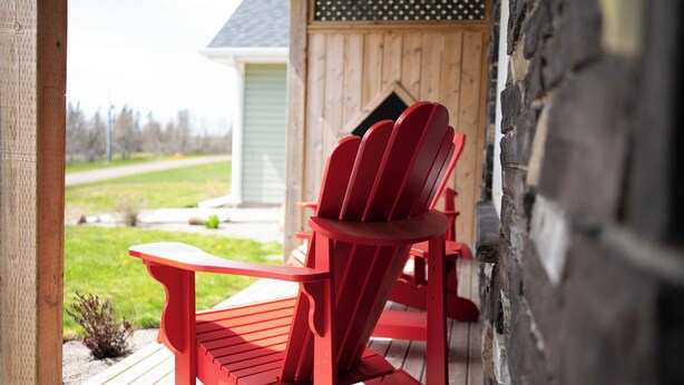 A red Adirondack chair on a wooden deck with a view of a house and a grassy yard.