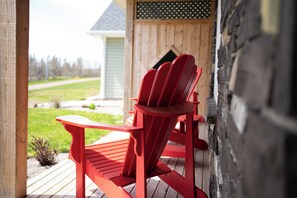 Punainen Adirondack-tyylinen tuoli puukannella, jolta avautuu näkymä taloon ja vihreälle nurmikolle.