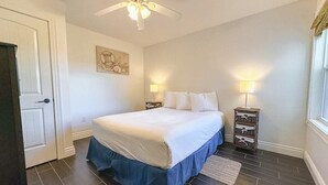 A bedroom with a bed, two bedside tables with lamps, a ceiling fan, and a door.