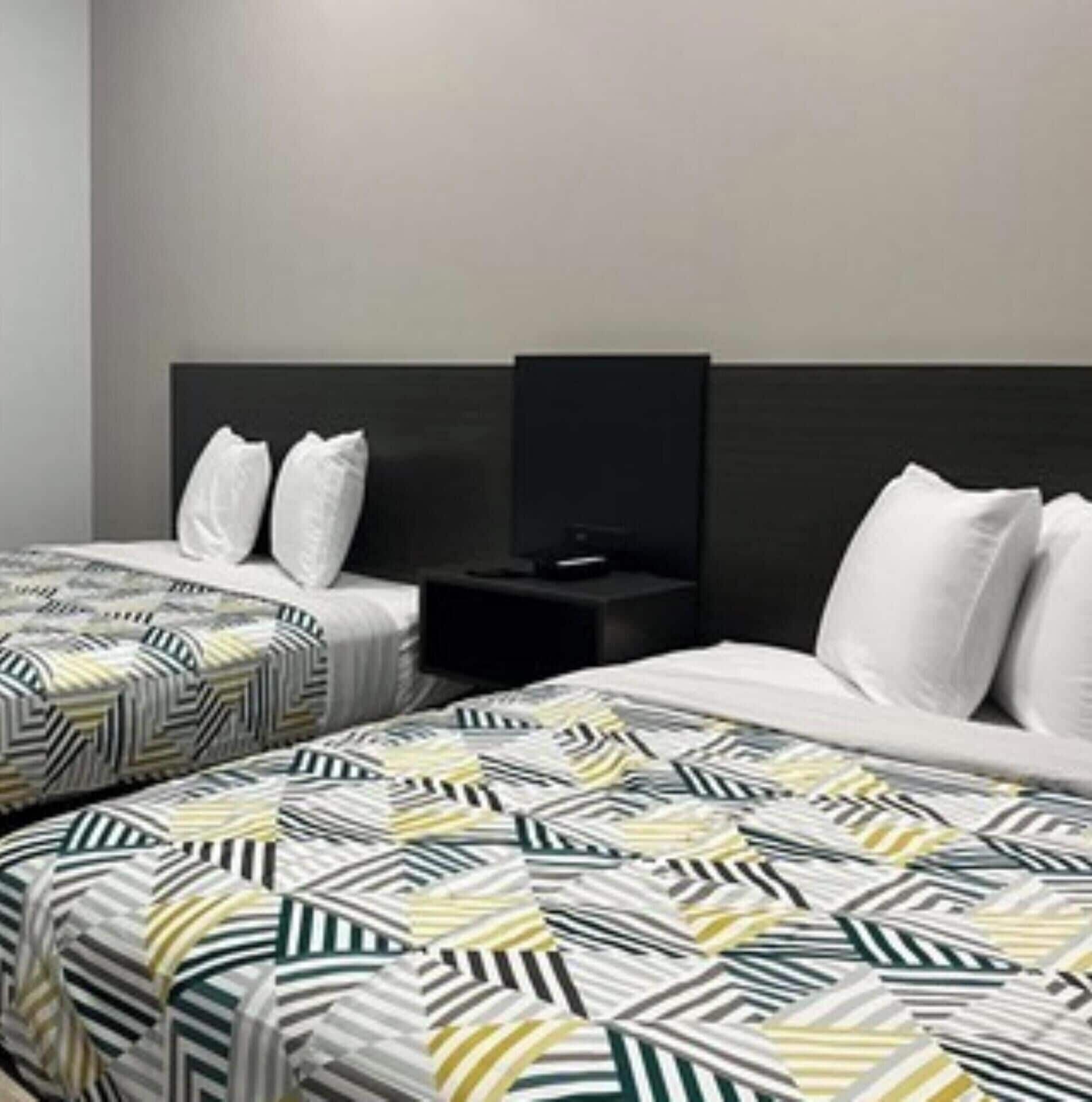 Una habitación de hotel con dos camas, cada una con una colcha estampada, cabeceros negros y un televisor de pantalla plana sobre un soporte negro.