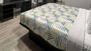Een net opgemaakt bed met een deken met een geometrisch patroon, een donker hoofdbord en een wit kussen.