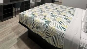A modern bedroom with a geometric patterned bedspread, a dark wooden headboard, and a white pillow.
