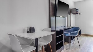 A modern room with a white desk, two white chairs, a dark wooden cabinet, and a blue chair. - Motel 6 Gonzales, La - Baton Rouge/Geismar/Prairieville I-10 (Gonzales)