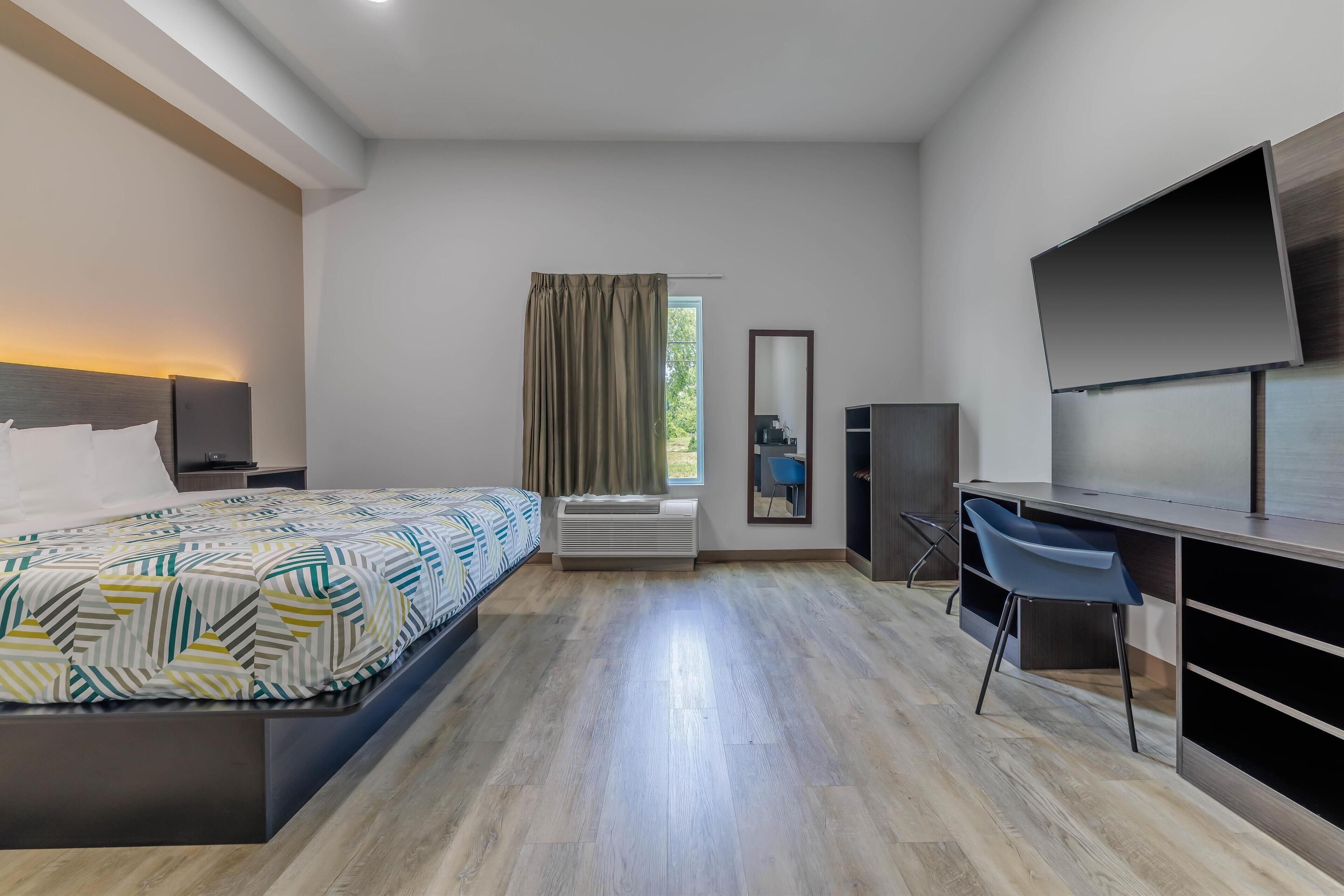 A modern hotel room with a large bed, a desk with a chair, a flat-screen TV, and a window with curtains.