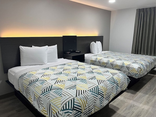 Habitación de hotel con dos camas, cada una con ropa de cama estampada, una mesita de noche con un reloj y un cabecero.