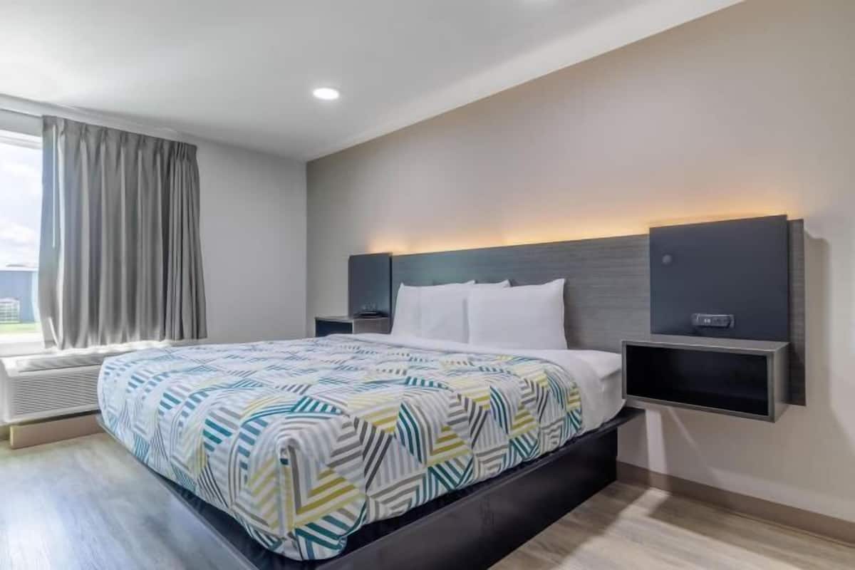 A modern hotel room with a large bed, a built-in TV, and a window with curtains.