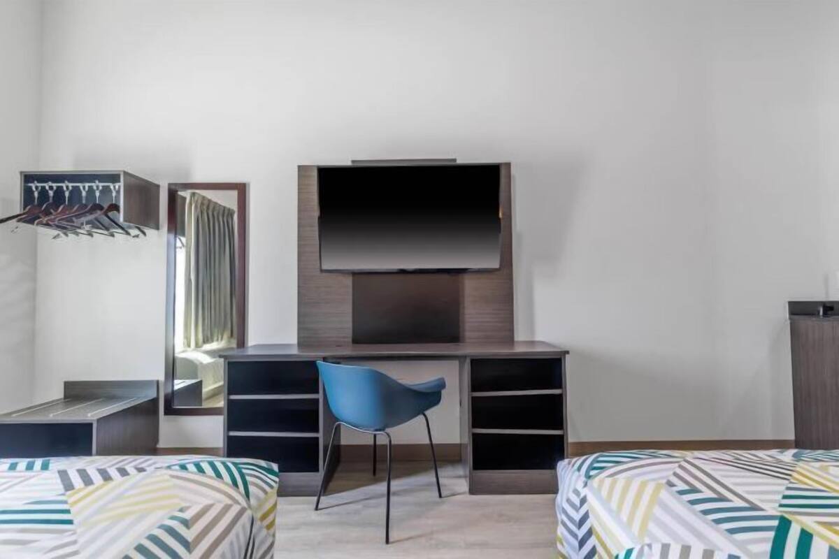 A bedroom with a bed, a desk with a chair, a TV, and a wardrobe.