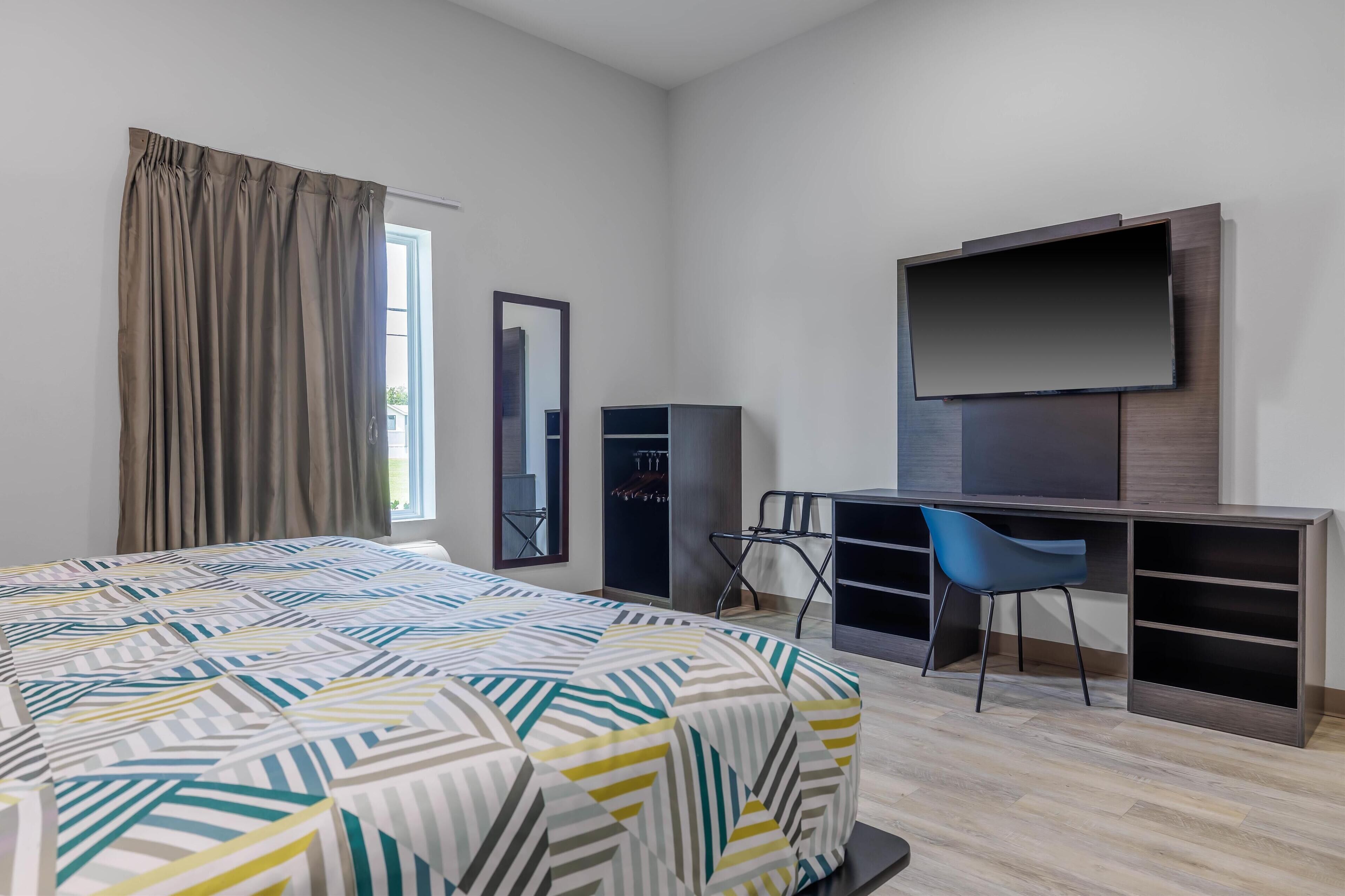A hotel room with a bed, a desk, a chair, a TV, a wardrobe, and a mirror.