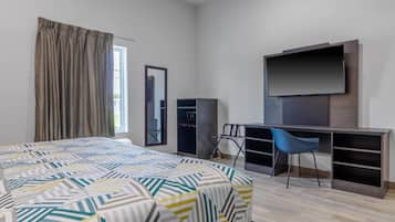 A hotel room with a bed, a desk, a chair, a TV, a wardrobe, and a mirror.