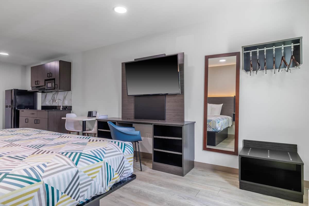 A modern hotel room with a bed, desk, TV, and a mirror.