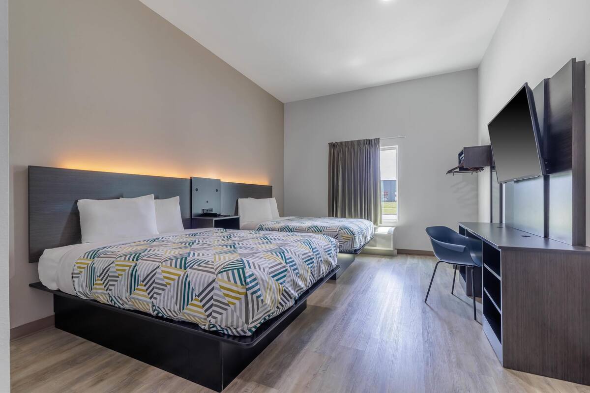 A modern hotel room with two beds, a desk, a chair, and a TV.