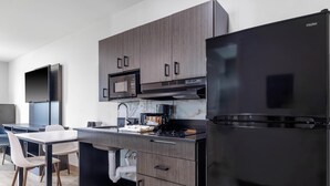 A modern kitchen with dark wood cabinets, a black refrigerator, a microwave, and a coffee machine. - Studio 6 Gonzales, La - Baton Rouge/Geismar/Prairieville I-10 (Gonzales)