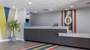 A reception area with a modern design, featuring a reception desk, a potted plant, and a colorful striped carpet. - Studio 6 Gonzales, La - Baton Rouge/Geismar/Prairieville I-10 (Gonzales)
