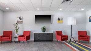 A modern waiting area with a flat-screen TV, red chairs, a grey cabinet, and a colorful striped rug. - Studio 6 Gonzales, La - Baton Rouge/Geismar/Prairieville I-10 (Gonzales)