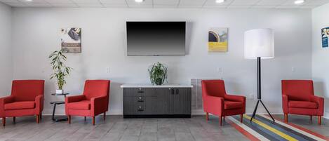 A modern waiting area with a flat-screen TV, red chairs, a grey cabinet, and a colorful striped rug.