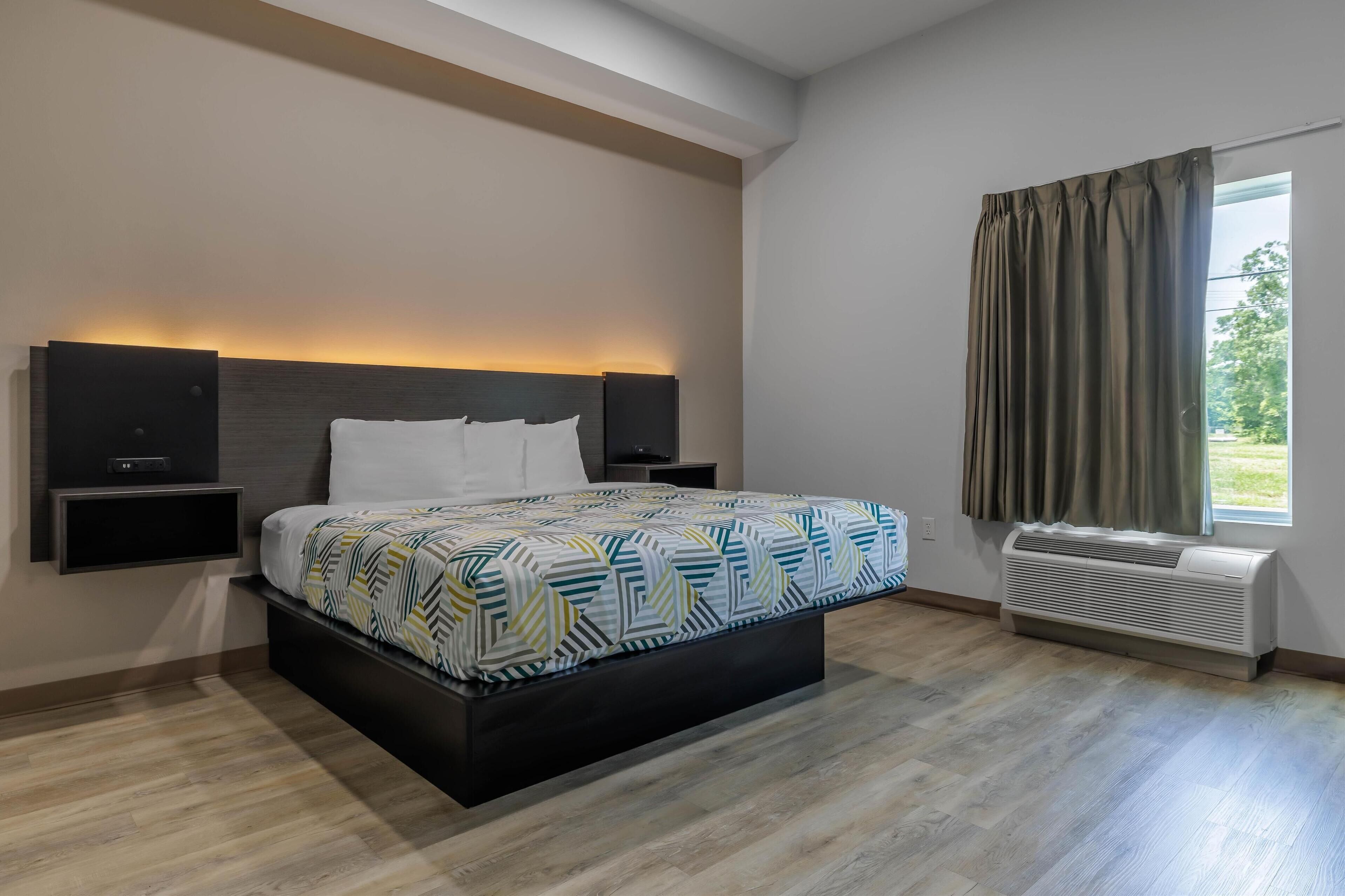 Una habitación de hotel moderna con una cama grande, altavoces integrados, una ventana con cortinas y un equipo de aire acondicionado.