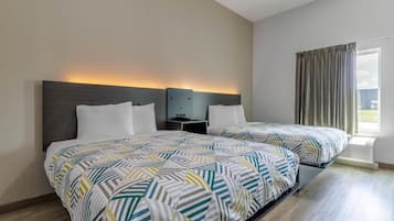 A hotel room with two beds, a nightstand, a wall-mounted lamp, and a window with curtains.