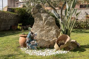 A garden with a large rock formation, a small figurine, and potted plants.