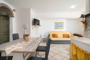 A room with a dining table, chairs, a sofa, a television, and a framed picture on the wall.