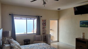 A bedroom with a bed, a ceiling fan, a window with curtains, a TV, and a painting on the wall. - Incredible views!! 1 bedroom condo with large terrace #504 at Vista Encantada! (El Divisadero)