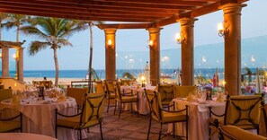 An outdoor dining area with tables set for guests, overlooking a beach.
