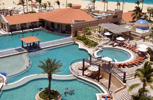 A resort with multiple swimming pools, sun loungers, and a beach area.