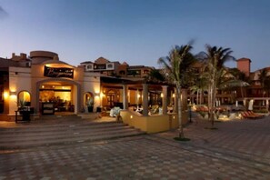 A hotel with a well-lit entrance, outdoor seating area, and palm trees.