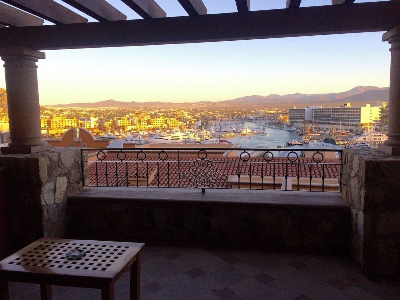 Ein Balkon mit Blick auf eine Stadtlandschaft, eine Steinsitzbank und ein Tisch mit einer Flasche.