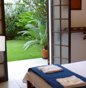 A room with a bed, a potted plant, and a view of a green garden.
