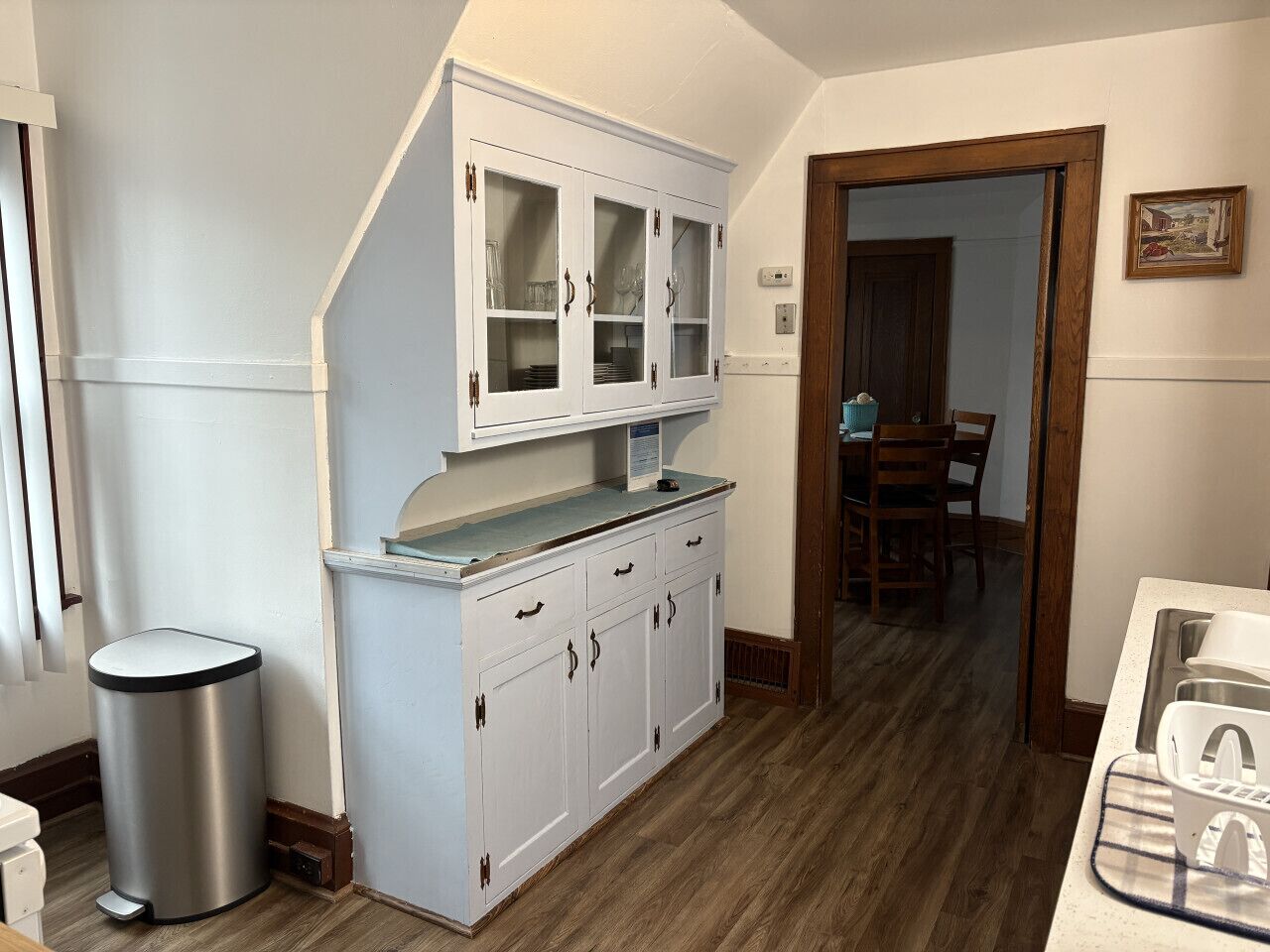 Una cocina con armarios blancos, un bote de basura de acero inoxidable y piso de madera.
