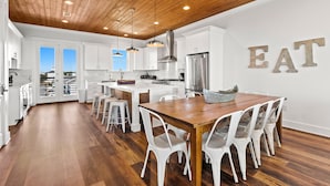 A modern kitchen with white cabinetry, a wooden ceiling, and a dining area with a wooden table and white chairs.