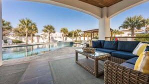 A covered outdoor area with a pool, wicker furniture, and a view of palm trees and buildings.