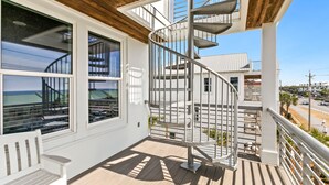 A spiral staircase with a metal railing, large windows with views of the ocean, and a wooden deck.