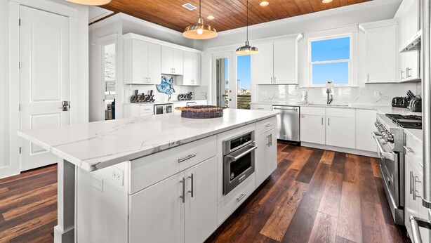 A modern kitchen with white cabinetry, a large island, stainless steel appliances, and a wooden ceiling.