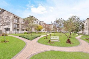 Stroll through the beautifully landscaped courtyard, featuring a curved pathway and a central seating area with a bench.
