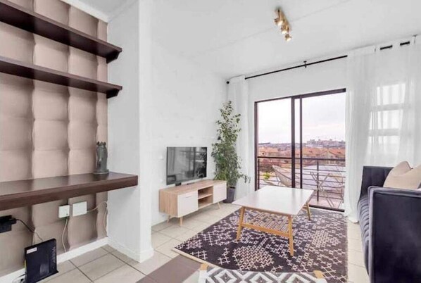 Relax in a spacious living room with a large window offering a view of the city, a flat-screen TV, and a comfortable sofa.
