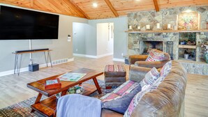 Un salón amplio con chimenea de piedra, techo de madera y televisor de pantalla plana montado en la pared.
