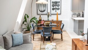 Una sala de estar moderna con una mesa de comedor redonda, sofá gris y una cocina con armarios y electrodomésticos.