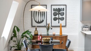 Un comedor con una mesa redonda, sillas, un aparador de madera y dos obras de arte abstractas enmarcadas en la pared.