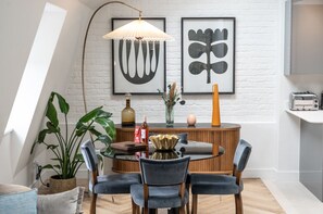 A dining area with a round table, chairs, a lamp, and framed artwork on the wall.