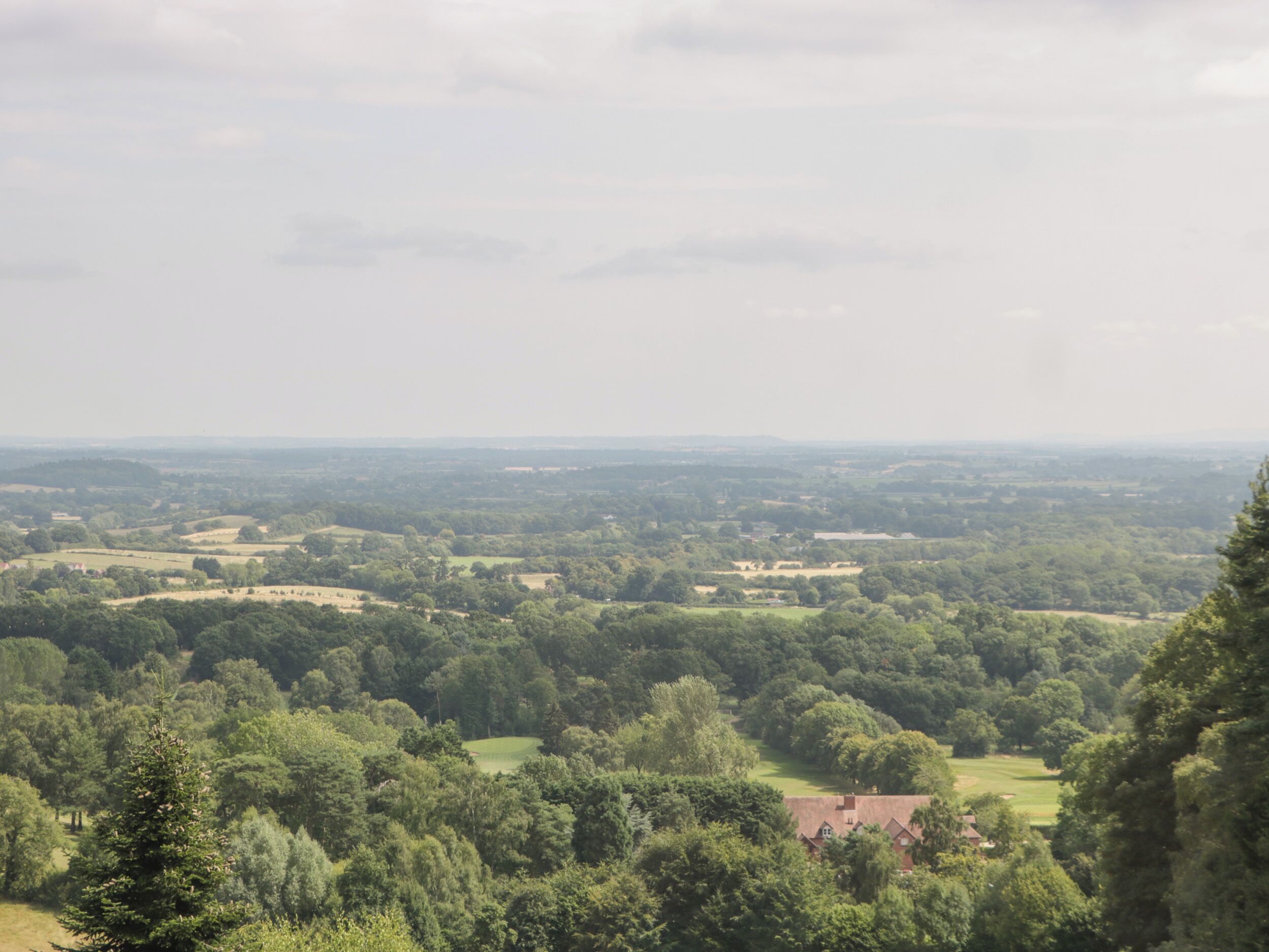 Une vue panoramique d’un paysage verdoyant, avec des collines ondoyantes et des bâtiments dispersés.