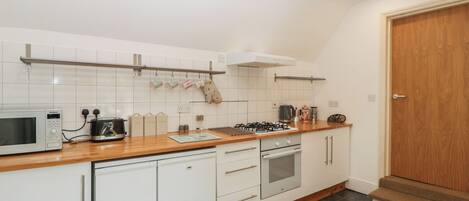 A modern kitchen with white cabinets, a microwave, a gas stove, and a coffee machine.