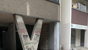 Une entrée d’immeuble ornée d’un grand « » en béton et de divers graffitis.