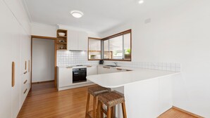 A modern kitchen with white cabinetry, a central island, and a built-in oven. - Lonnie Getaway - Point Lonsdale (Point Lonsdale)