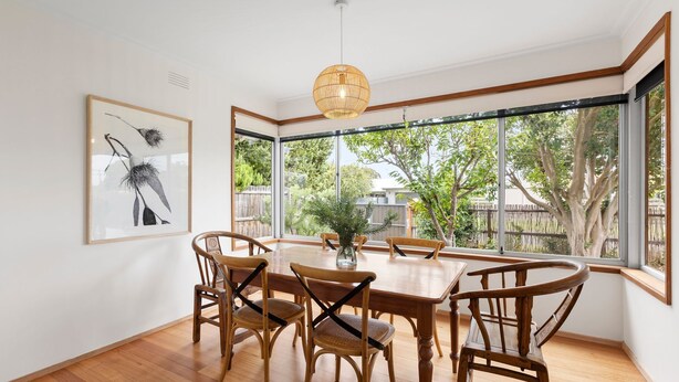 A dining area with a wooden table and chairs, large windows, and a hanging light fixture. - Lonnie Getaway - Point Lonsdale (Point Lonsdale)