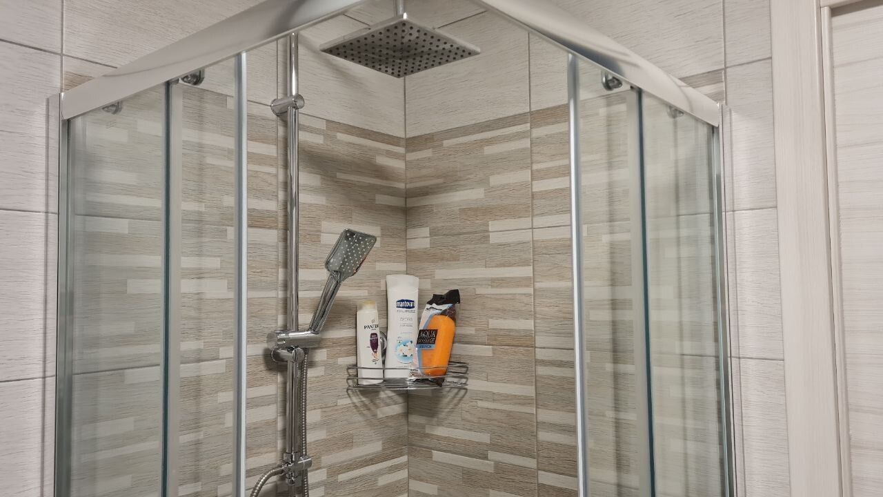 A modern shower with a glass enclosure, a handheld showerhead, and a shelf with toiletries.