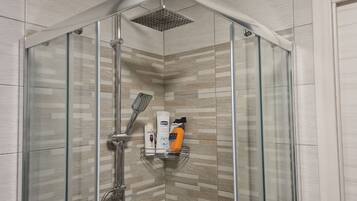 A modern shower with a glass enclosure, a handheld showerhead, and a shelf with toiletries.