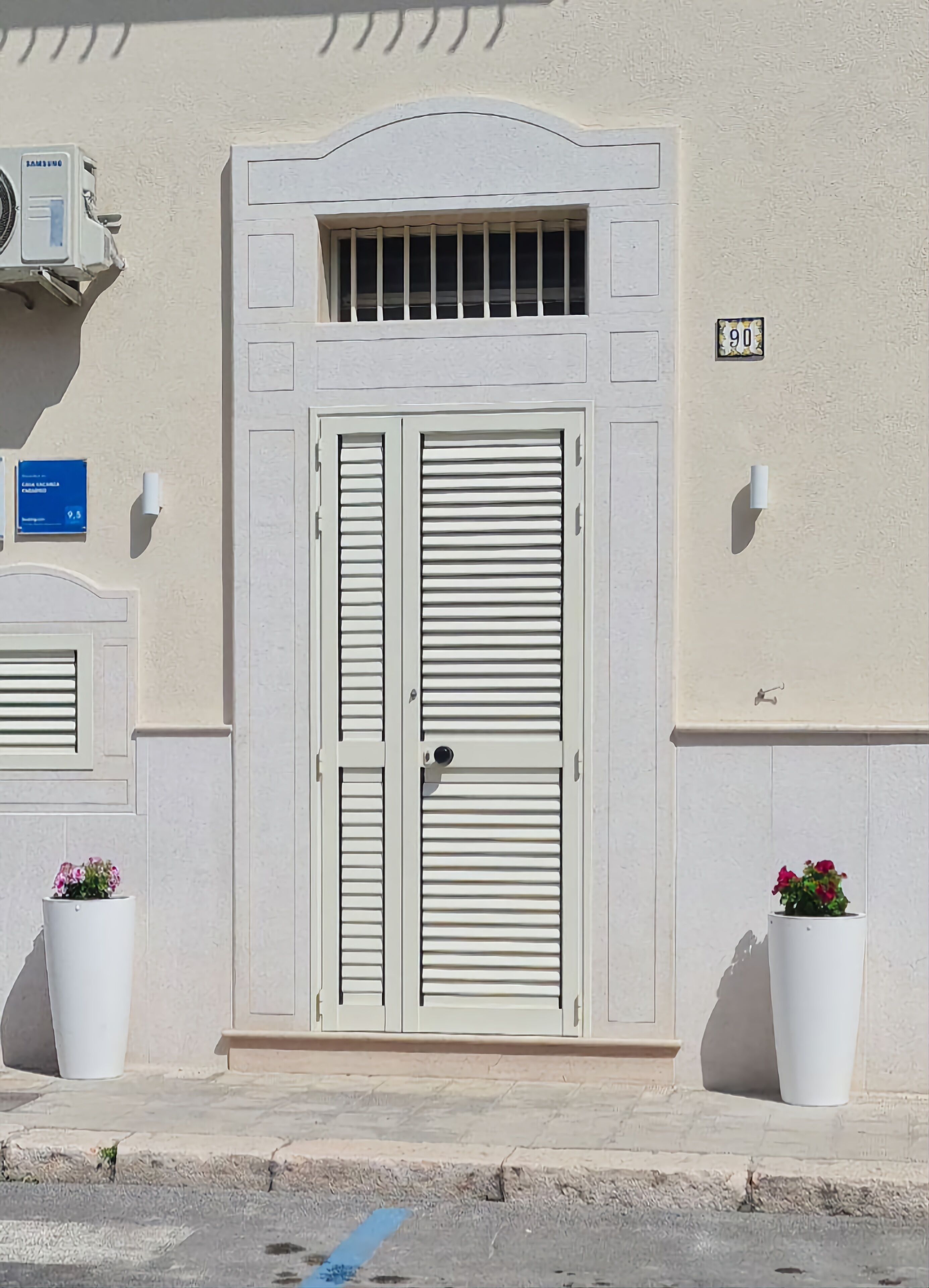 A building facade with a double door, a small window with bars, and two potted plants.