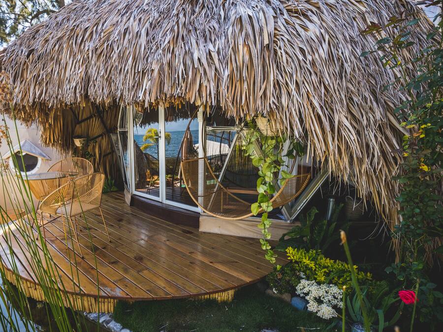 A thatched-roof outdoor seating area with a wooden deck, wicker chairs, and a hanging chair.
