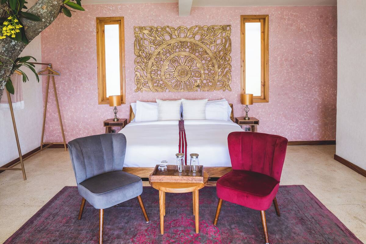 Un dormitorio con cama, dos sillas, una mesita y un adorno en la pared.